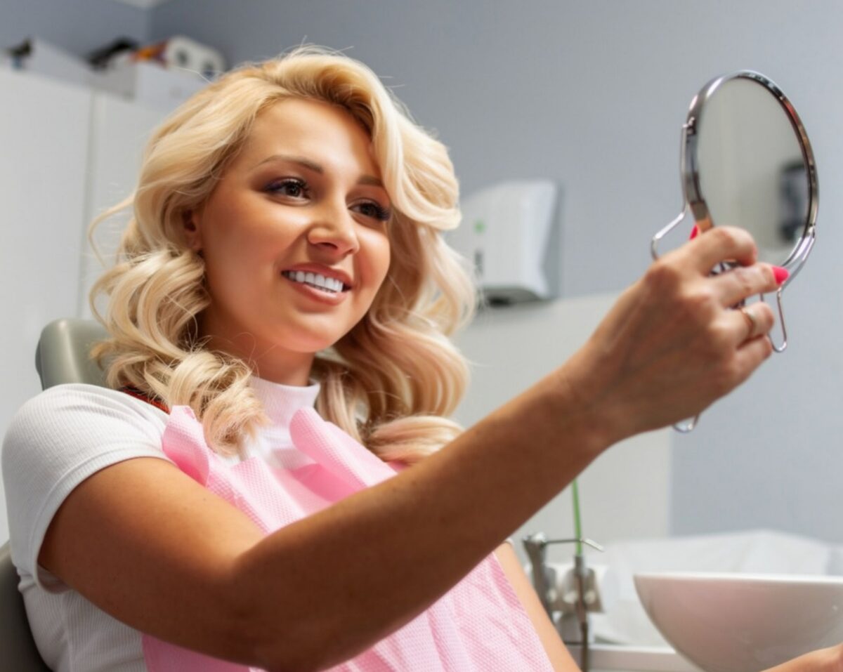 female dental patient holding a mirror admiring her smile